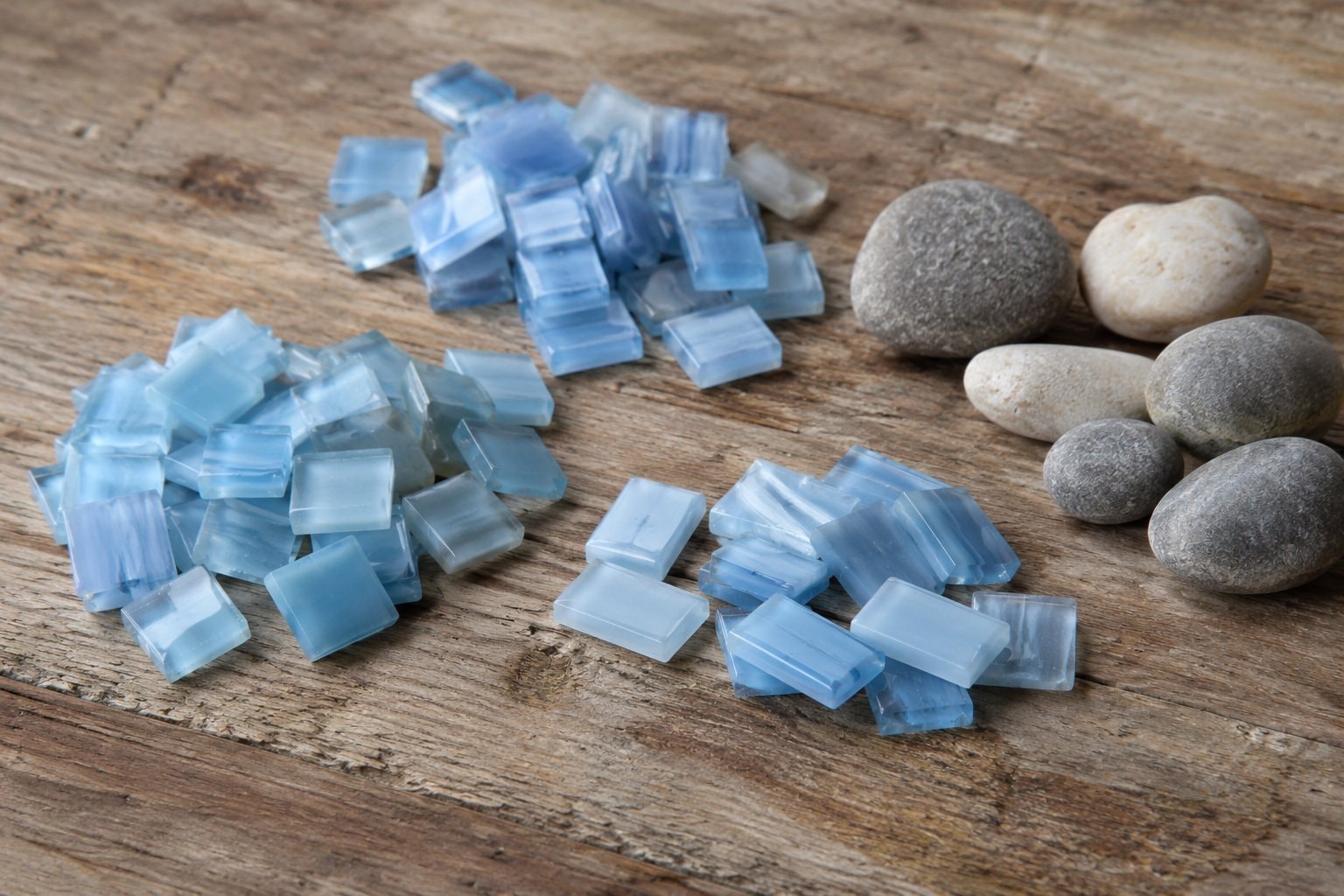 Loose pale-blue glass pieces and smooth pebbles on a wooden workbench.